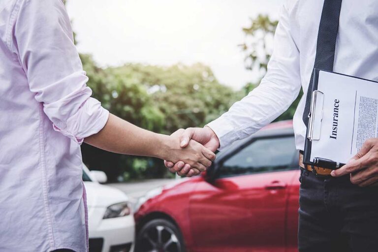 A close-up of a hand holding an auto insurance card inside a parked car.