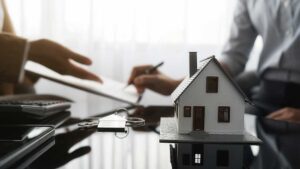 Adult reviewing suspicious account statements and an insurance policy at a kitchen table with a laptop and phone.