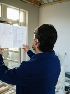 Homeowner reviews renovation plans and insurance papers beside construction materials in a partially remodeled room.